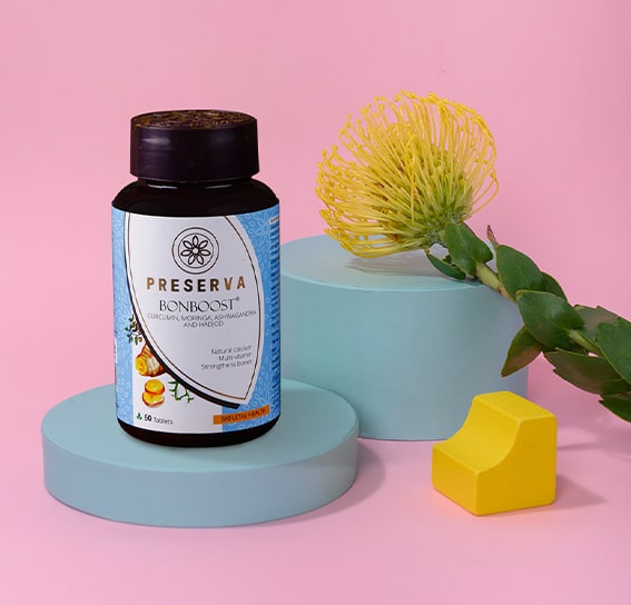 Bonboost Tablets on a blue round stand next to a yellow flower and a yellow object in a pink background setup.