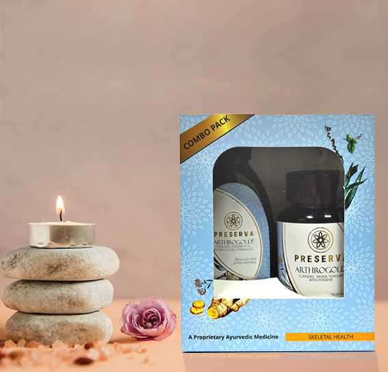 Arthrogold Tablets & Oil Combo Pack next to a small candle on three decorative stones with a flower and some pebbles on the table.